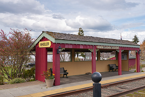 Benches under a covered waiting area next to train tracks. A sign on the covered waiting area says Wheeler.