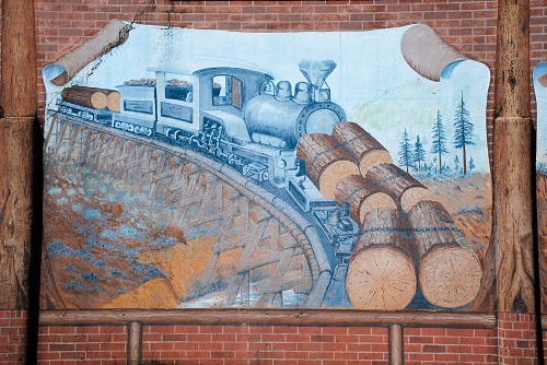Mural of train pushing logs down a rail road track in the forest.