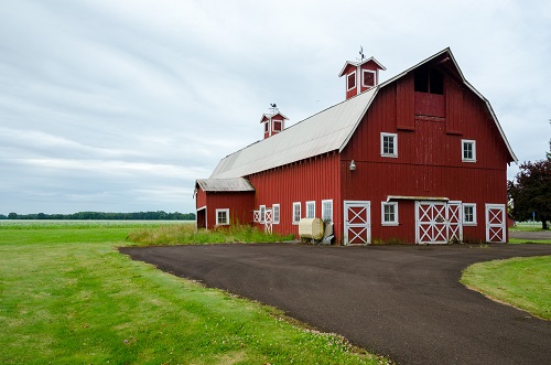 A 2-story barn with 2 chimneys or vents coming out of roof. A paved, curved driveway runs in front. Green lawn on sides.