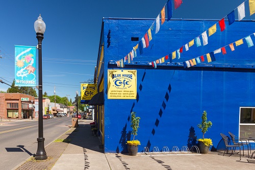 Bright blue painted concrete building with sidewalk in front. Colorful flags strung across patio area. Blue House Cafe sign.