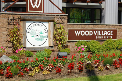Welcome sign & flowers. On the left "Welcome to Wood Village" & On the right "Wood Village Town Center."