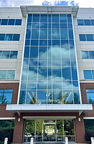 A multi-story building with a large glass facade reflecting the blue sky and clouds.