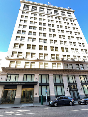 A tall, white building with many windows under a clear blue sky. The building has a classic architectural style with decorative cornices and appears to be in an urban setting.