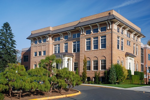 Wood-Mar Hall at George Fox University in Newberg, Oregon. A historic brick academic building with tall arched windows, a central entrance, and surrounding mature trees.
