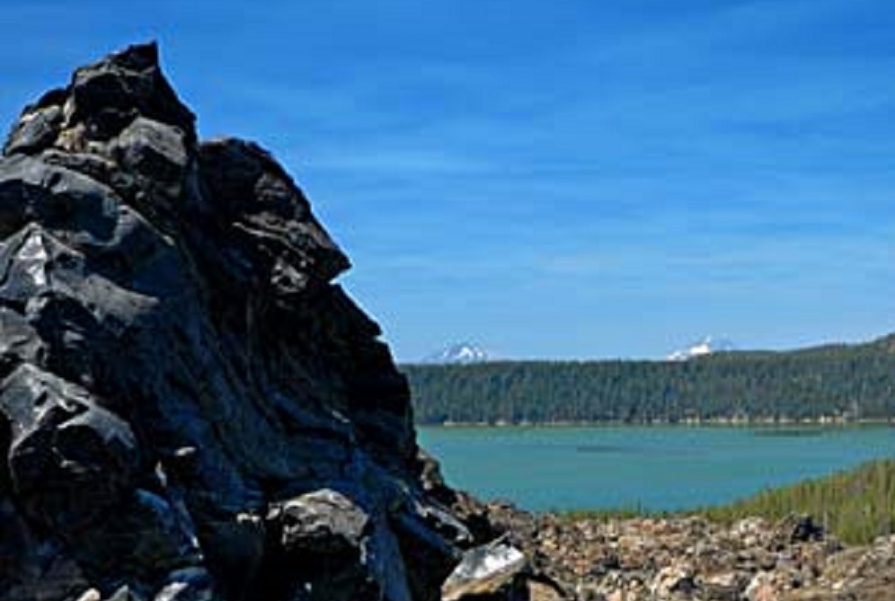 A jagged formation of dark volcanic rock rises on the left side of the image, with a calm blue lake stretching out behind it.
