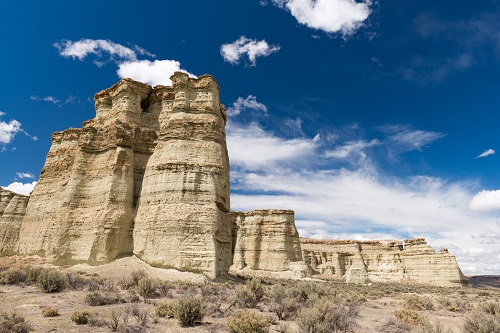Tall, light‑colored rock formations rise from a dry, shrub‑covered landscape under a deep blue sky.