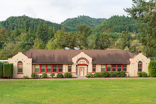 A single-story building with a curved, red-tiled roof and white stucco walls. The building has multiple red-framed windows and two prominent white arches flanking the central entrance, which is marked by a sign reading LIBRARY.