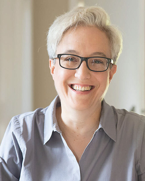 Tina Kotek has short white hair, is wearing glasses and a white shirt with black suit jacket.