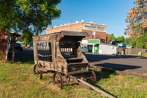 An old wooden wagon with SHANIKO painted on its side is displayed in the foreground. It rests on iron wheels and appears weathered, suggesting historical significance.