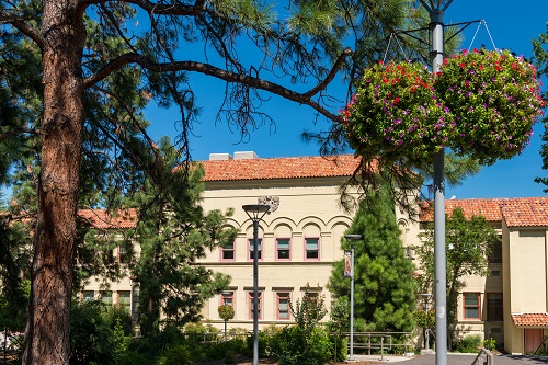 Two story building with a terra cotta roof sits behind evergreen trees.