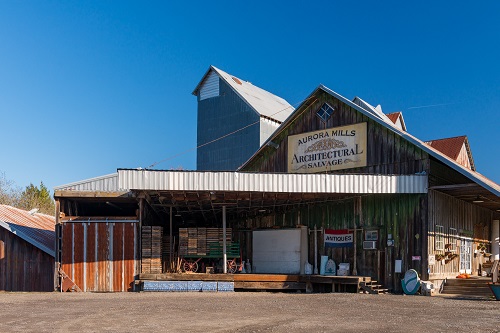 An old building in Aurora with a sign on the front that says Aurora Mills Architechtural Salvage. A banner reads Antiques below.