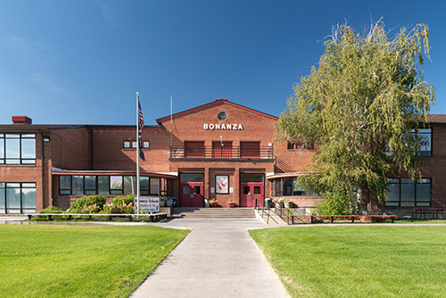 Two story brick building with grassy lawn in front, a flag pole and a tree.