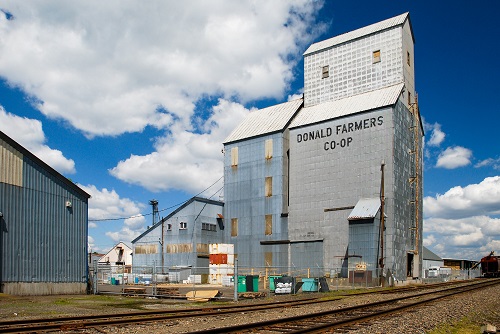 A grain elevator next to double train tracks with Donald Farmers Co-Op printed on the building's side.