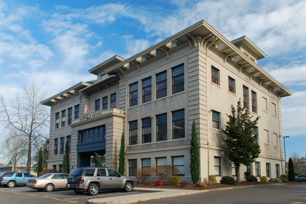 Historic brick school building with a symmetrical façade, arched entryway, and tall windows.