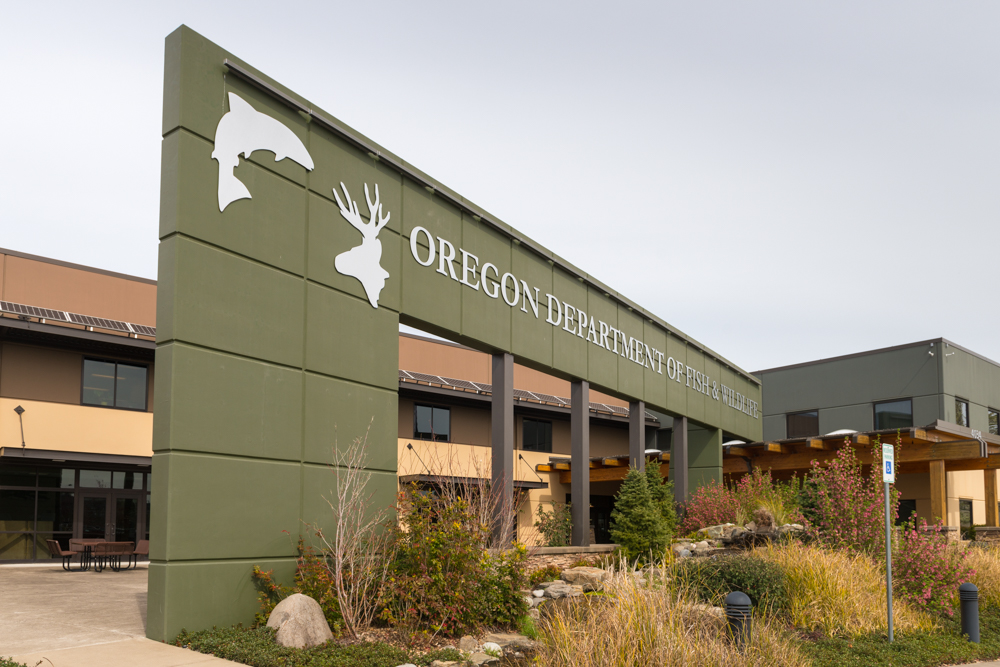 An archway with shapes of fish and deer and the name Oregon Department of Fish & Wildlife printed. The building behind is 2 stories with a flat roof.