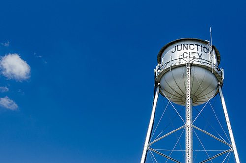 A classic white water tower with the words JUNCTION CITY painted in black on its tank.
