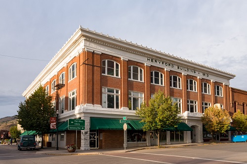Three-story brick, early commercial style building. Building takes up city block. Front door at an angle to corner of sidewalk.