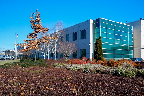 Exterior view of the Oregon State Lottery’s headquarts—a modern, two-story office building with a flat roof and light-colored façade, surrounded by landscaped greenery and a paved parking area
