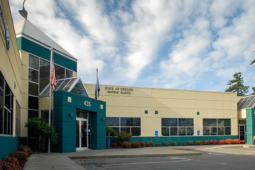 a modern, low‑rise, single‑story office building with light-colored façade and large windows, set amid a paved parking lot.