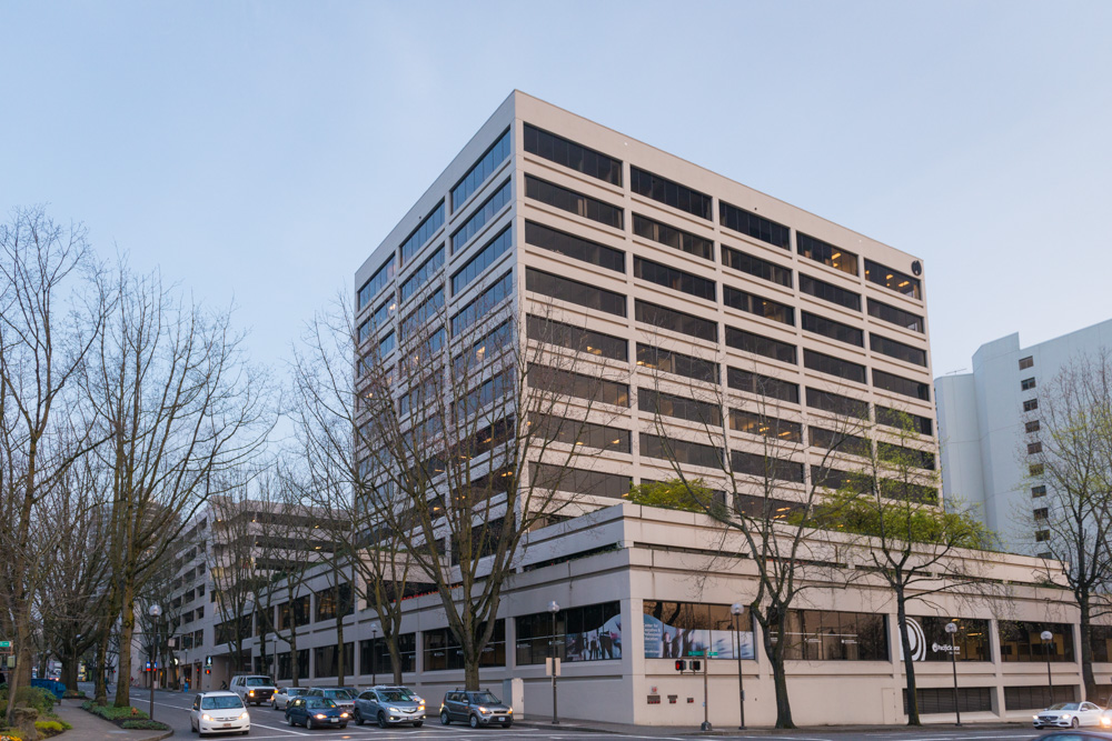Street‑level view of the Crown Plaza office complex at 1500 SW 1st Avenue in downtown Portland—an 11‑story, Class A mid‑century modern office building with a mostly flat roof, expansive rows of windows. 