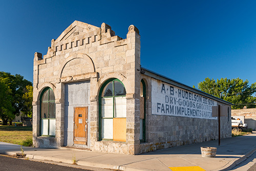 A historic stone building with arched windows and a sign reading A.B. Huddleston Co. Dry-Goods Groceries Farm Implements on its side. 
