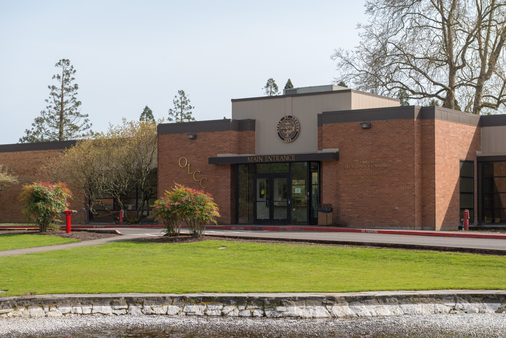 A mid‑century single-story brick and glass government office structure set back from the street with landscaped grounds.