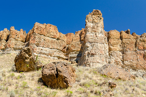 Layered rock formations and hoodoos rising from arid terrain in the Clarno Unit of John Day Fossil Beds