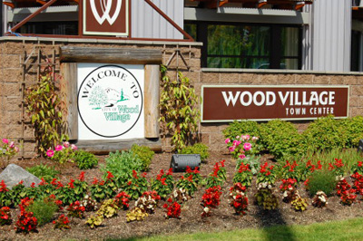Welcome sign & flowers. On the left a sign says Welcome to Wood Village