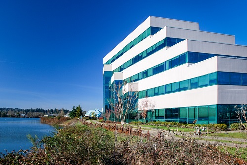 A five‑story contemporary office building with reflective glass windows and a curved façade, situated at the northeast edge of a small lake.