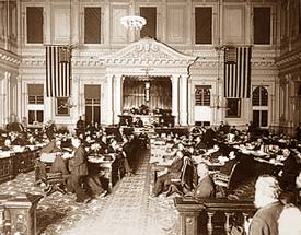 Photo of the Senate Chamber in 1895 in Salem Oregon. There are dozens of men at desks in a large, high ceiling room.