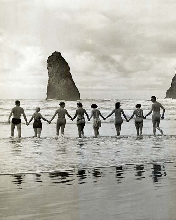 Line of 8 people holding hands walk into the ocean surf in their swim suits in 1940.