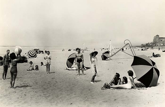 Beach goers play in the sand, toss a beach ball and lounge under umbrellas.