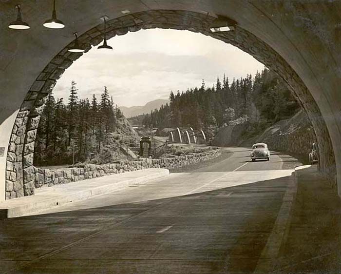 Stone tunnel opens up on highway with a 1940s car driving away.