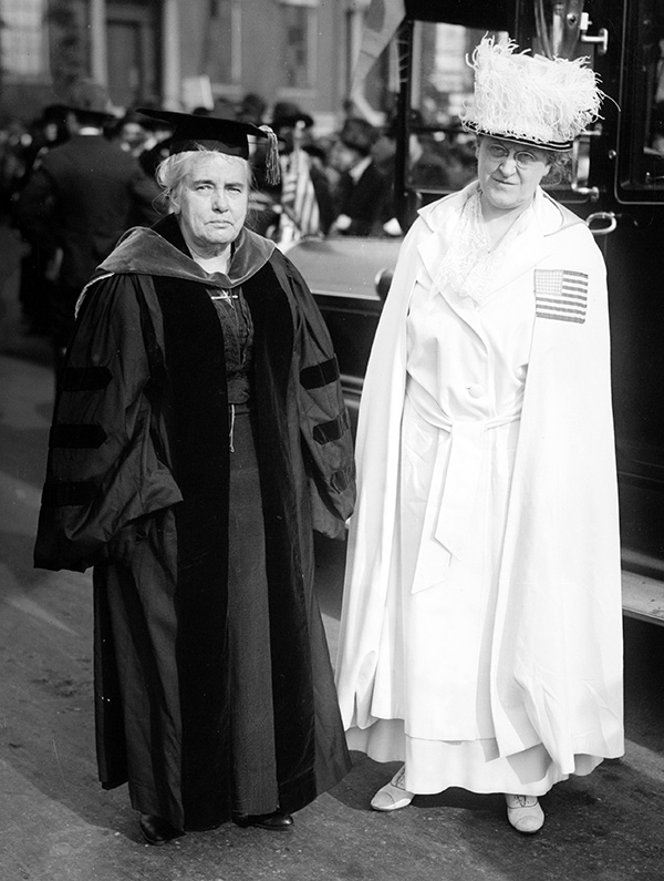 Photo of Carrie Chapman Catt in dark robes & Anna Howard Shaw in white robes.