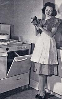 Woman in dress and apron in front of an oven in the kitchen holds a jar of canned beans.