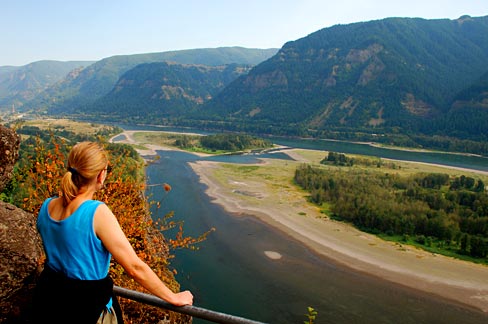 Woman stands at view point with hands on railing looking out over Columbia River.