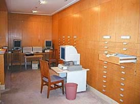 East alcove walled with wooden drawers and housing 2 desks, 3 chairs and 3 computer terminals for accessing microforms.