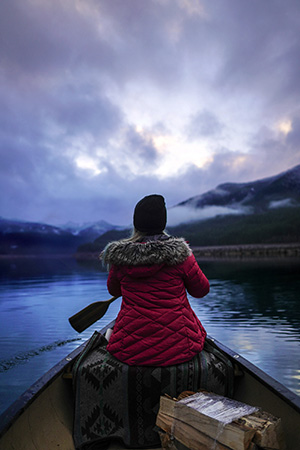 A woman in a warm jacket paddles a boat on a lake on a cloudy day.