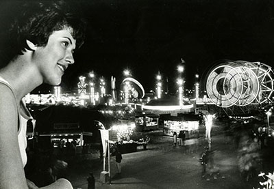 A woman looks at the bright lights of the State Fair at night