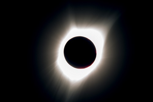 Photo of the sun during an eclipse shows a dark circle in the middle with a blaze of light around it.