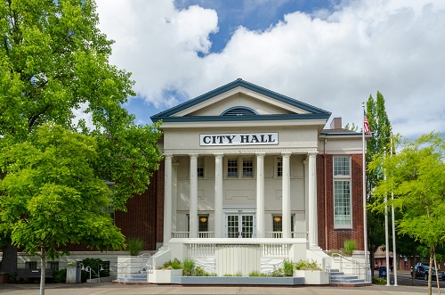 3 story historic City Hall building in colonial style with 6 pillars holding up the overhang above front door. Brick walls.