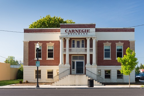 The Carnegie Building, built in 1911, of brick and stone with a stairway leading to the 2nd floor and a deck above the door.