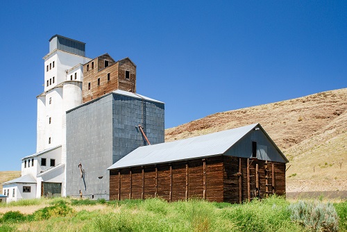 A grain elevator with a concrete building attached & another, smaller log building attached to that.