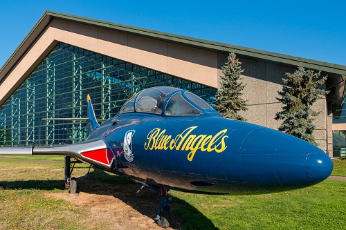 A jet known as a Grumman F9F-8, airplane flown by the Blue Angels. "Blue Angels" is written in script on the side nose of plane.