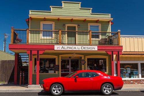 2-story building with porch on 2nd level. A red sports car is parked in front. Sign on building says Alpaca by Design.