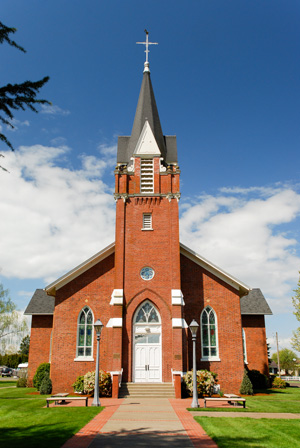 Brick church built in the Gothic Revival Style. Includes lofty spire, pointed arch openings, steeply pitched gable roof. Spire is surmounted by a Latin cross. Main entry is flanked by buttresses with sandstone coping. Rose Window fitted with stained glass is above the arched entry.