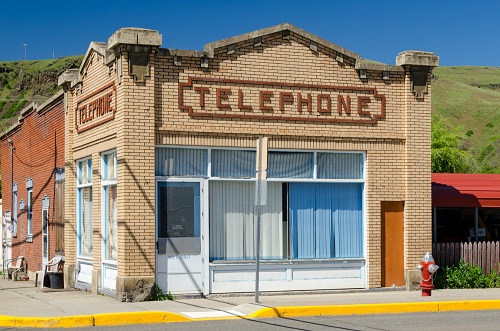 Single story cream colored brick building on street corner. The word "Telephone" in red brick on 2 sides above windows.